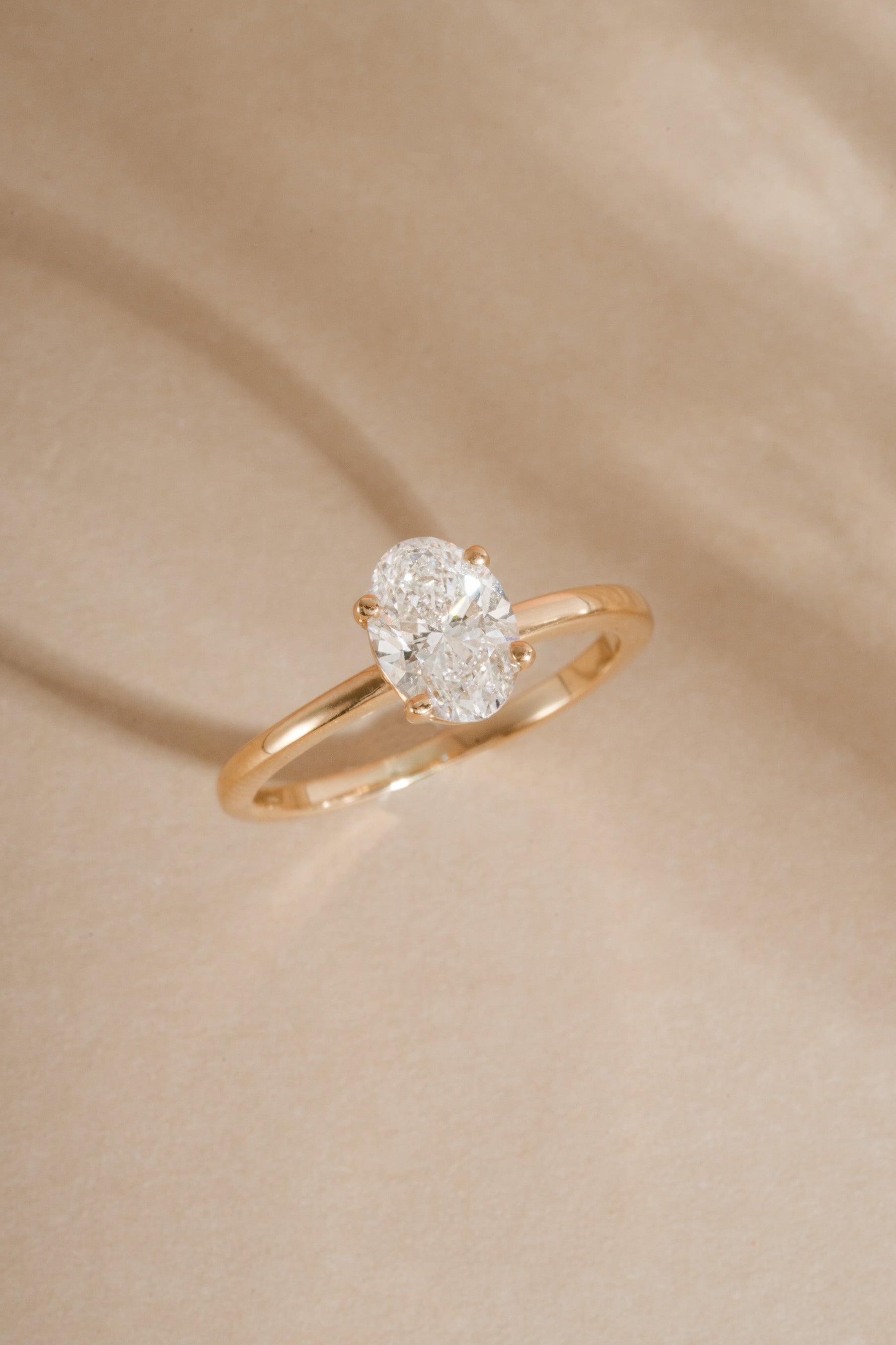 Close up of solid 14k yellow gold oval solitaire lab diamond ring with neutral background