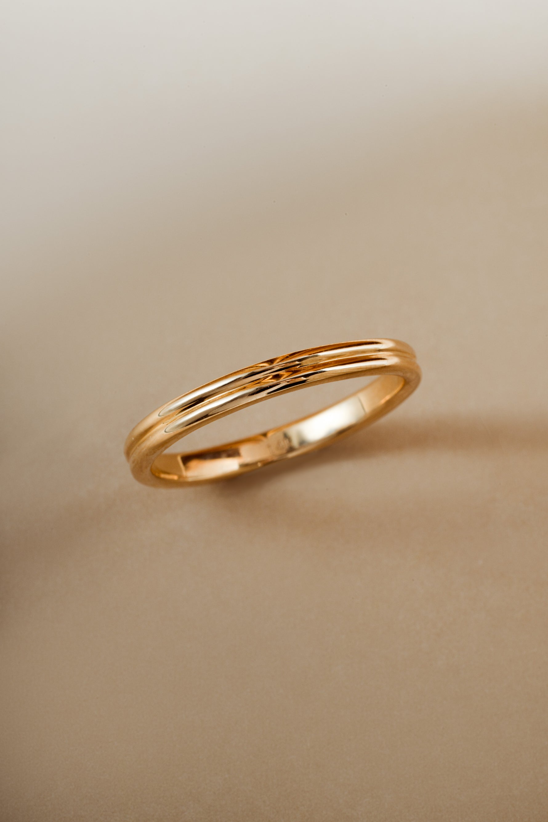 Solid gold double band wedding ring angled on a beige background