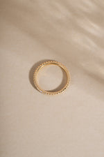 14K solid gold eternity diamond ring with small stones on a beige fabric background