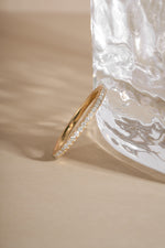 Solid gold lab grown diamond eternity ring on a beige surface next to a textured glass object