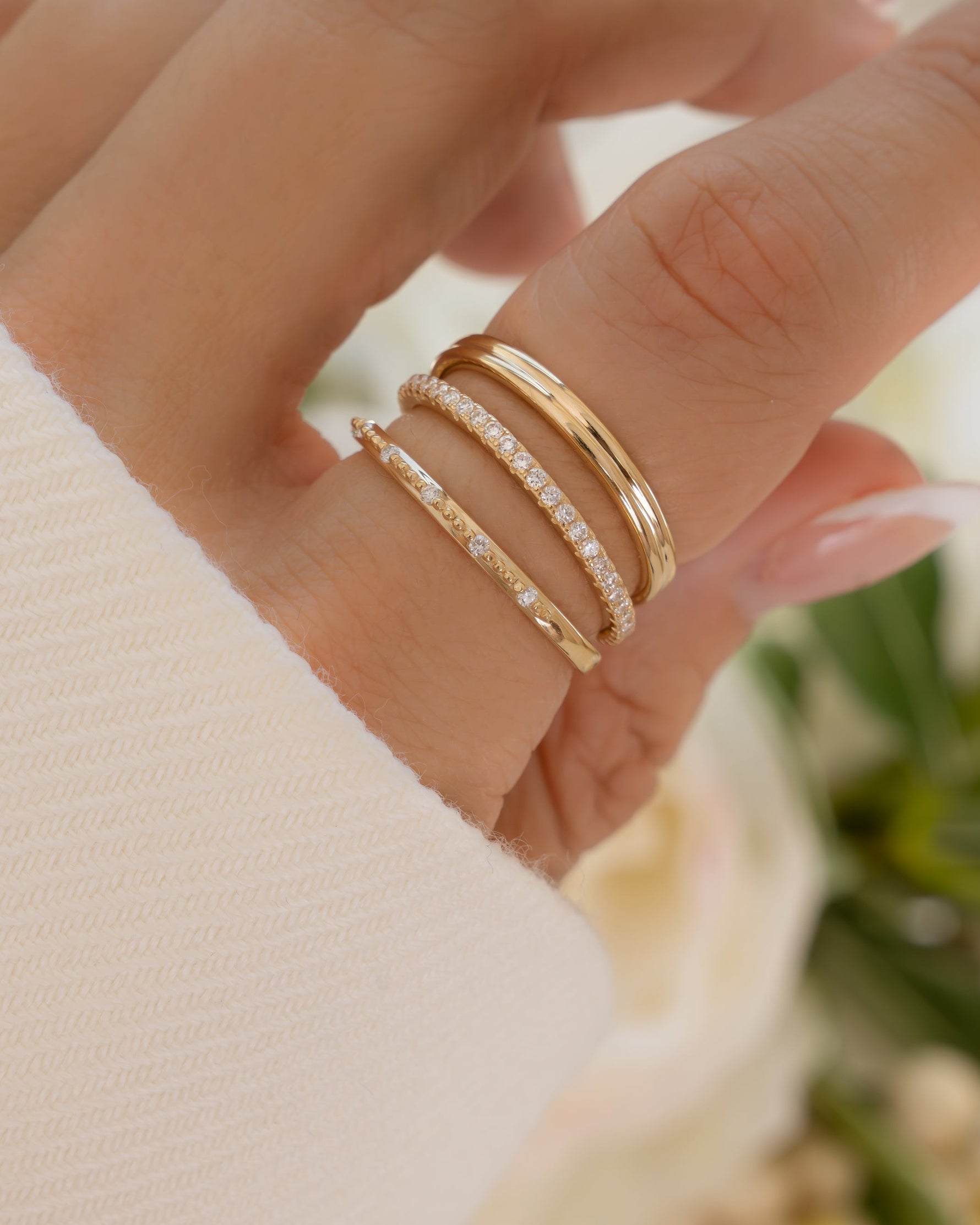 Close-up of hand wearing fine jewelry solid gold diamond rings with a blurred floral background