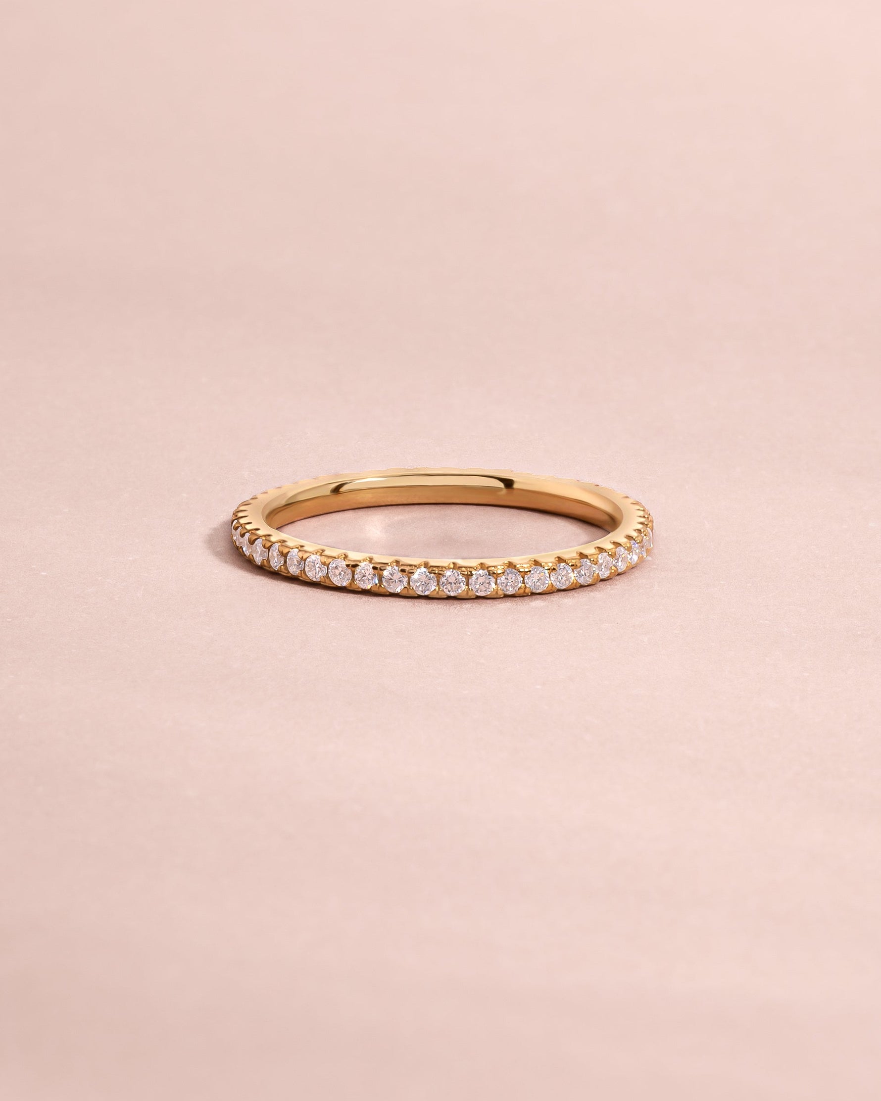 Solid gold diamond eternity ring with small pave stones on a light pink background