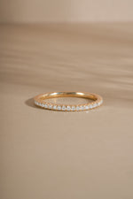 Gold eternity diamond engagement ring with tiny diamonds on a beige background