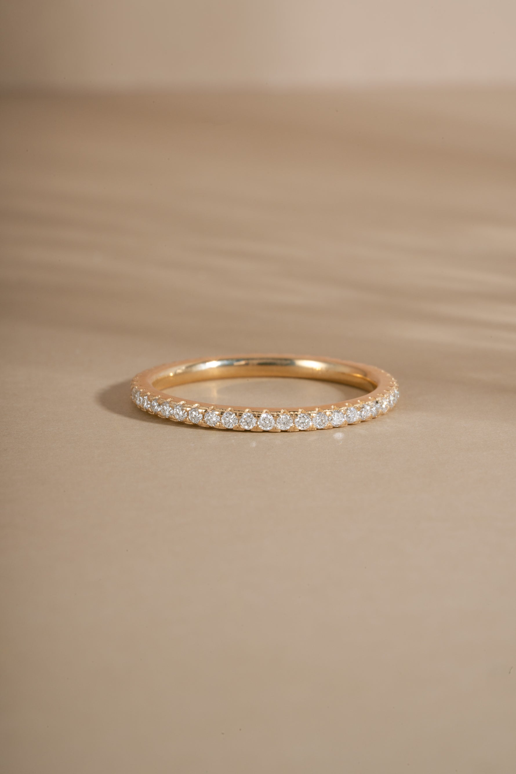 Gold eternity diamond engagement ring with tiny diamonds on a beige background