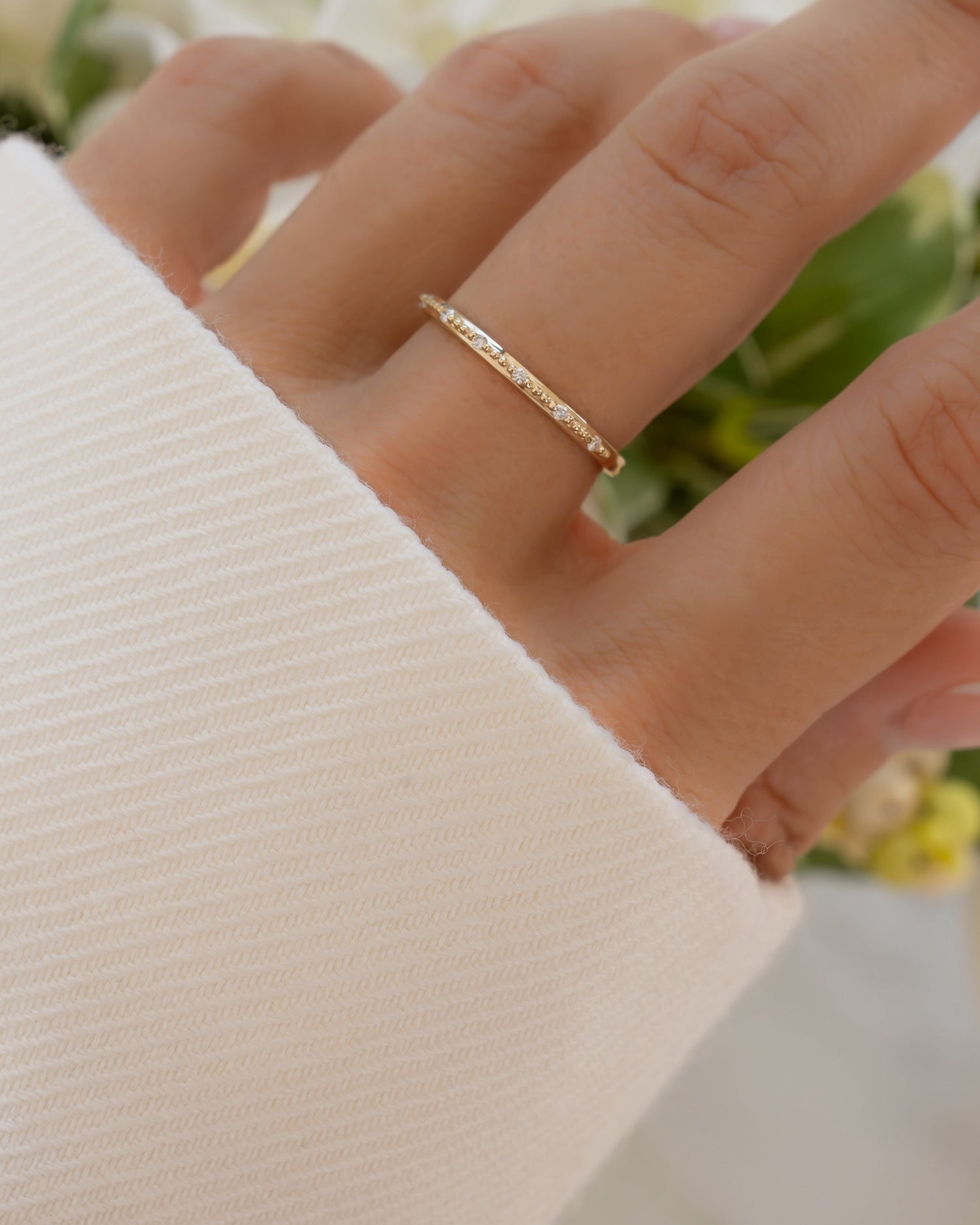 Close-up of a hand wearing a fine jewelry 14K solid gold stacking ring with a blurred floral background