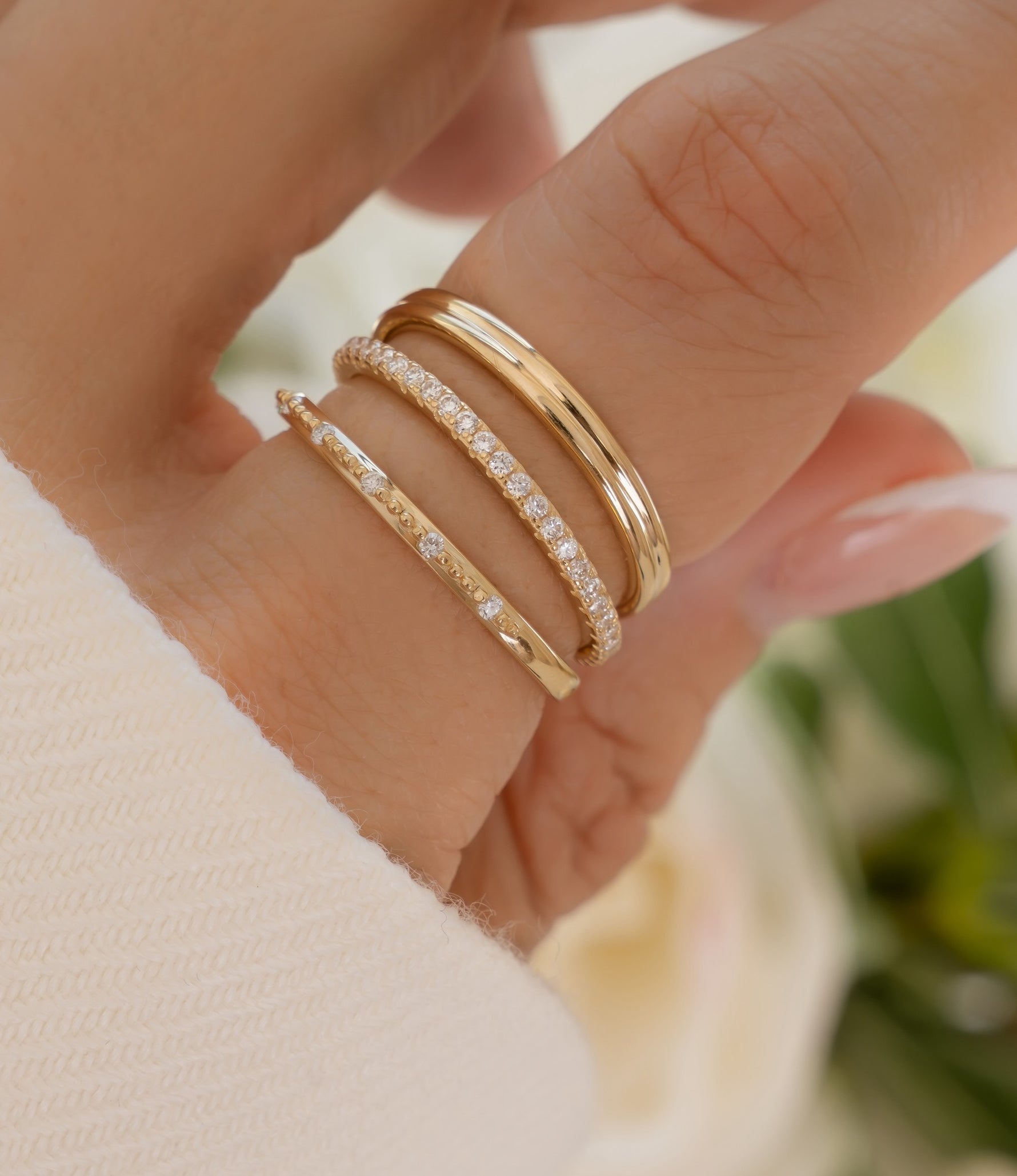 Three slim gold rings, including one pavé-set with small clear stones, worn on a person's finger.