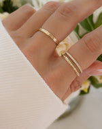 Hand wearing a minimal diamond stacking ring crafted in 14K solid gold styled with fine jewelry rings with a blurred floral background