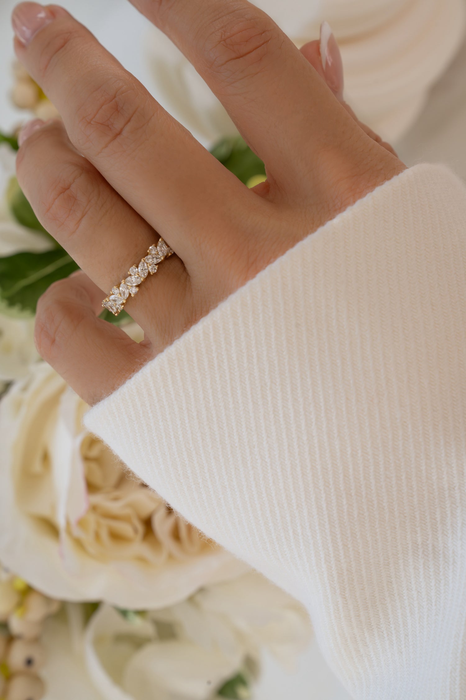 Hand wearing a 14K solid gold diamond ring with multiple diamonds a blurred floral background
