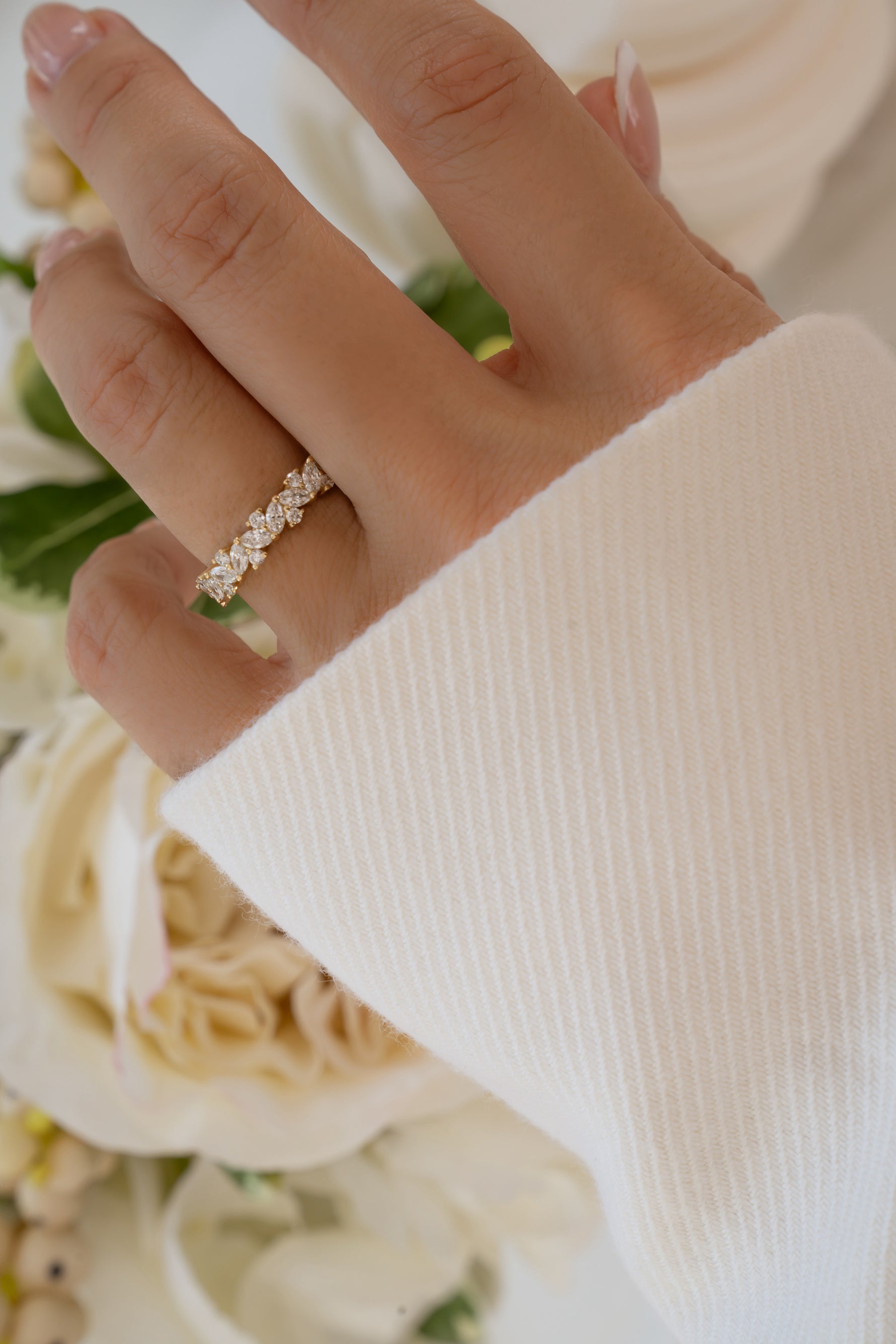 Hand wearing a 14K solid gold diamond ring with multiple diamonds a blurred floral background