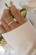 Close-up of a hand wearing a 14K solid gold multi stone lab grown diamond ring with a blurred floral background