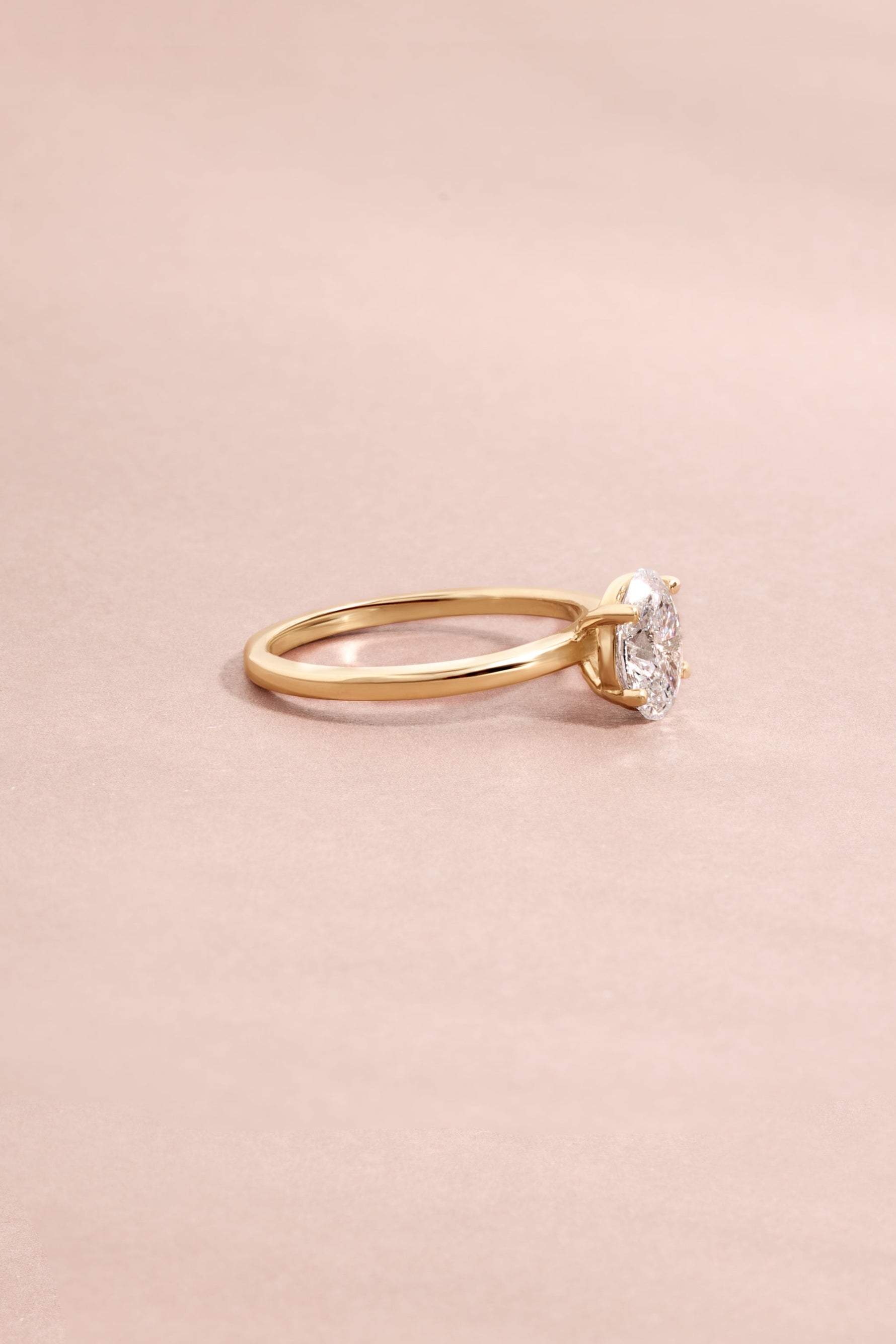 Side of oval cut 14K solid gold diamond ring on light pink background