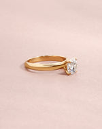 Side view of solid gold ring with a solitaire round diamond on a light pink background