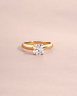 Round lab diamond solitaire ring set in solid 14k gold on light pink background