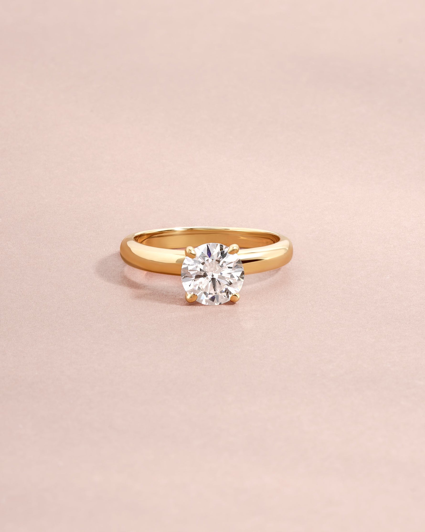 Round lab diamond solitaire ring set in solid 14k gold on light pink background