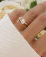 Solid 14k gold round diamond solitaire ring worn on hand with blurred floral background