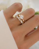 Hand wearing a 14K solid gold ring with a multi stone diamond engagement band against a blurred floral background