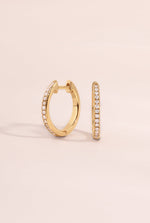 Side view of 14K solid gold pavé lab-grown diamond huggie earrings by Sami Jewels on a neutral background.