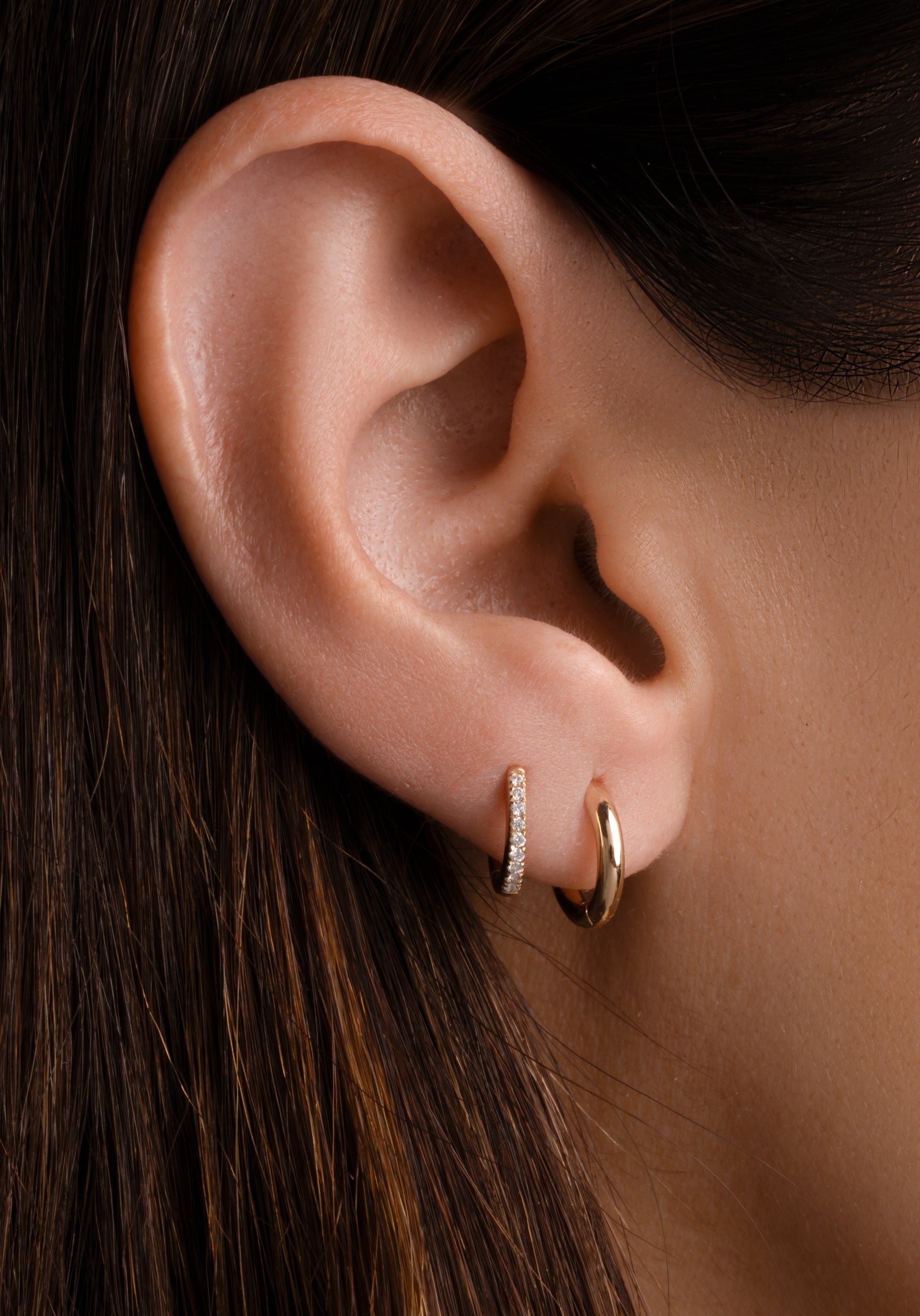 Close-up of an ear wearing two solid gold hoop earrings