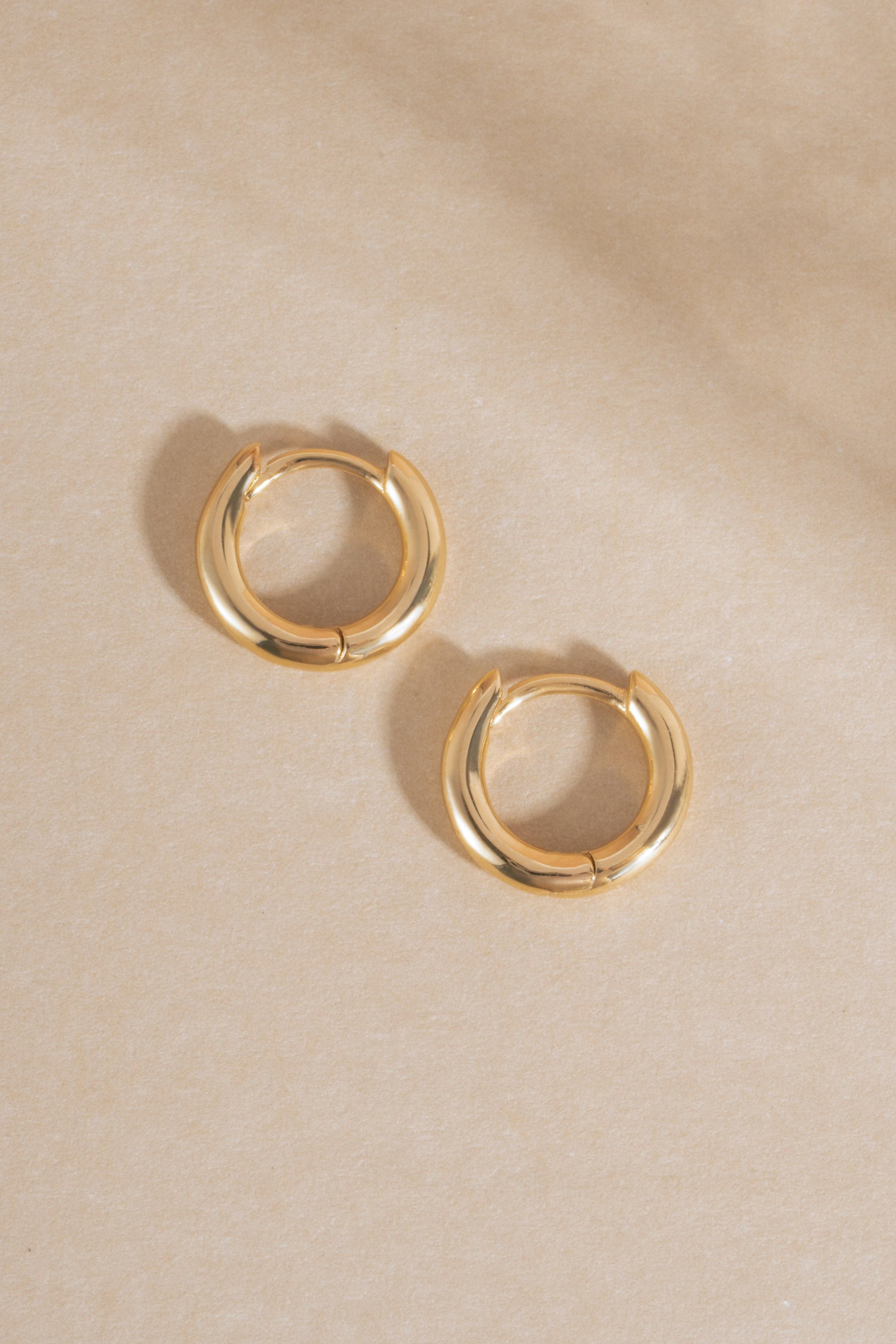 14K solid gold simple huggie hoops on neutral background