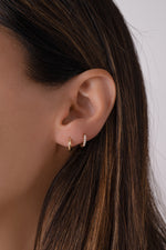 Close-up of a model wearing solid gold hoop earrings layered with diamond huggies with a neutral background