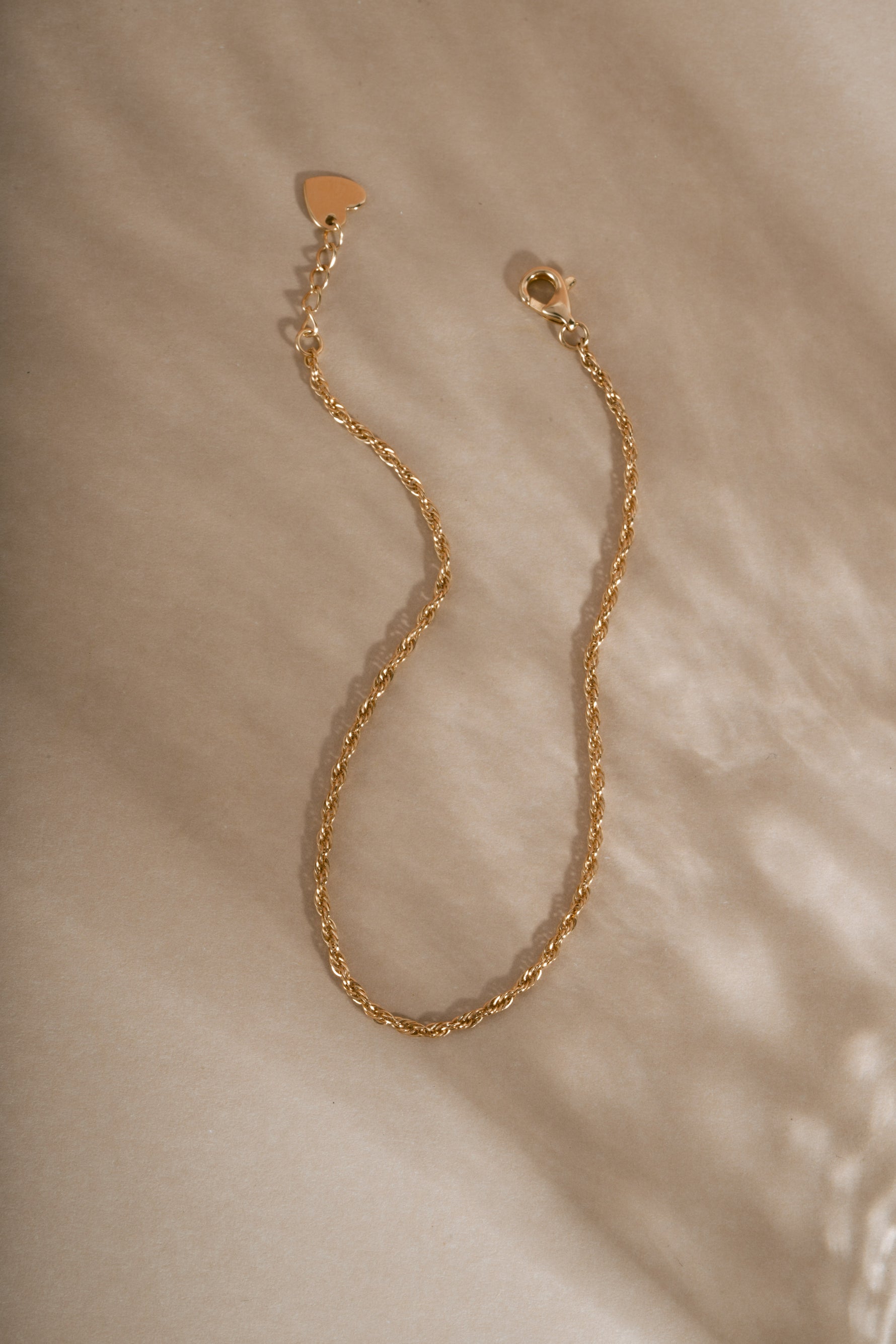Fine 14K solid gold twisted rope chain bracelet with lobster clasp and extension chain detail on neutral beige background