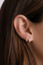 Close-up of an ear wearing a 14k solid gold hoop earring layered with dainty diamond huggies