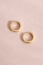 14K solid gold hoop earrings flat lay on a pink background
