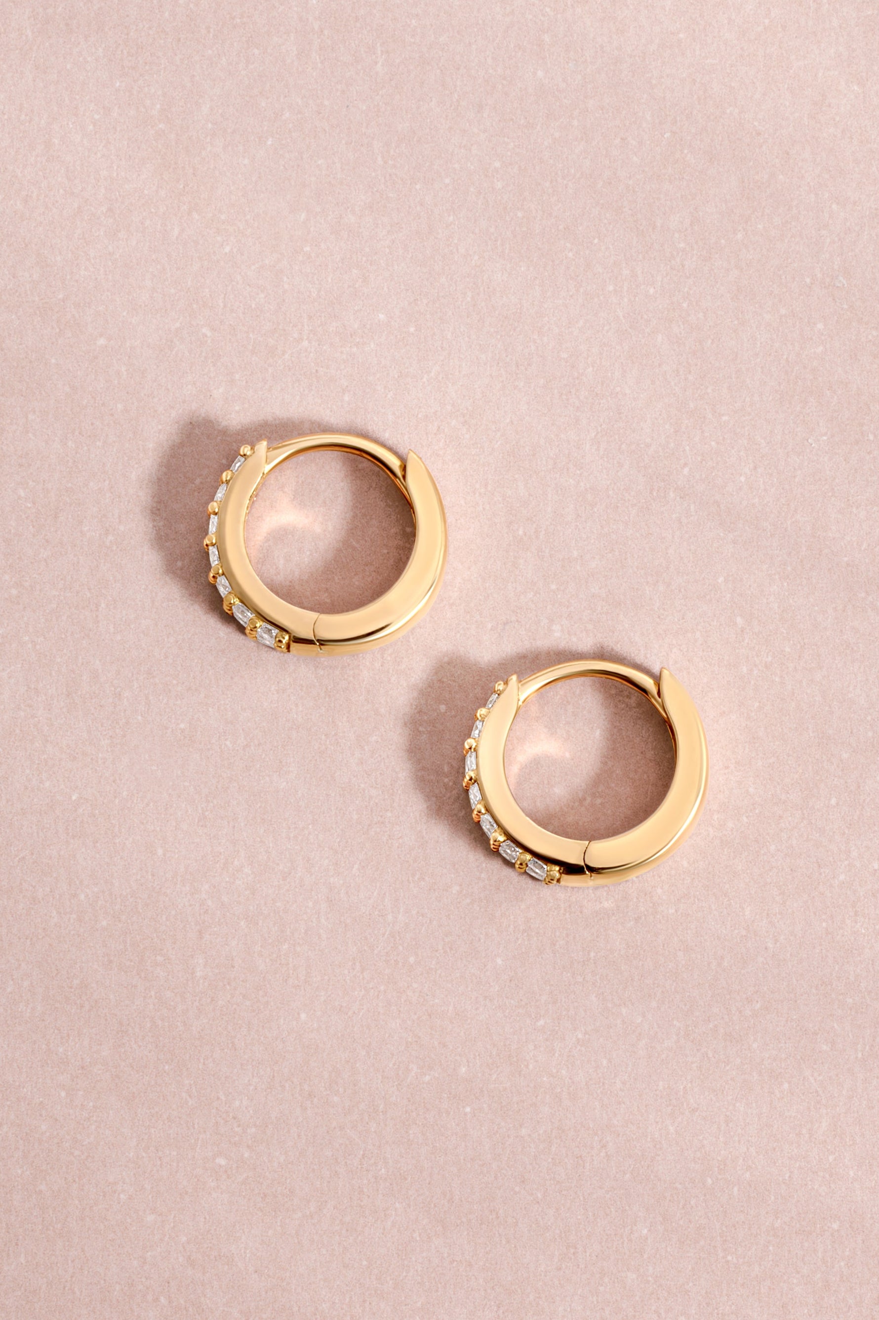 14K solid gold hoop earrings flat lay on a pink background