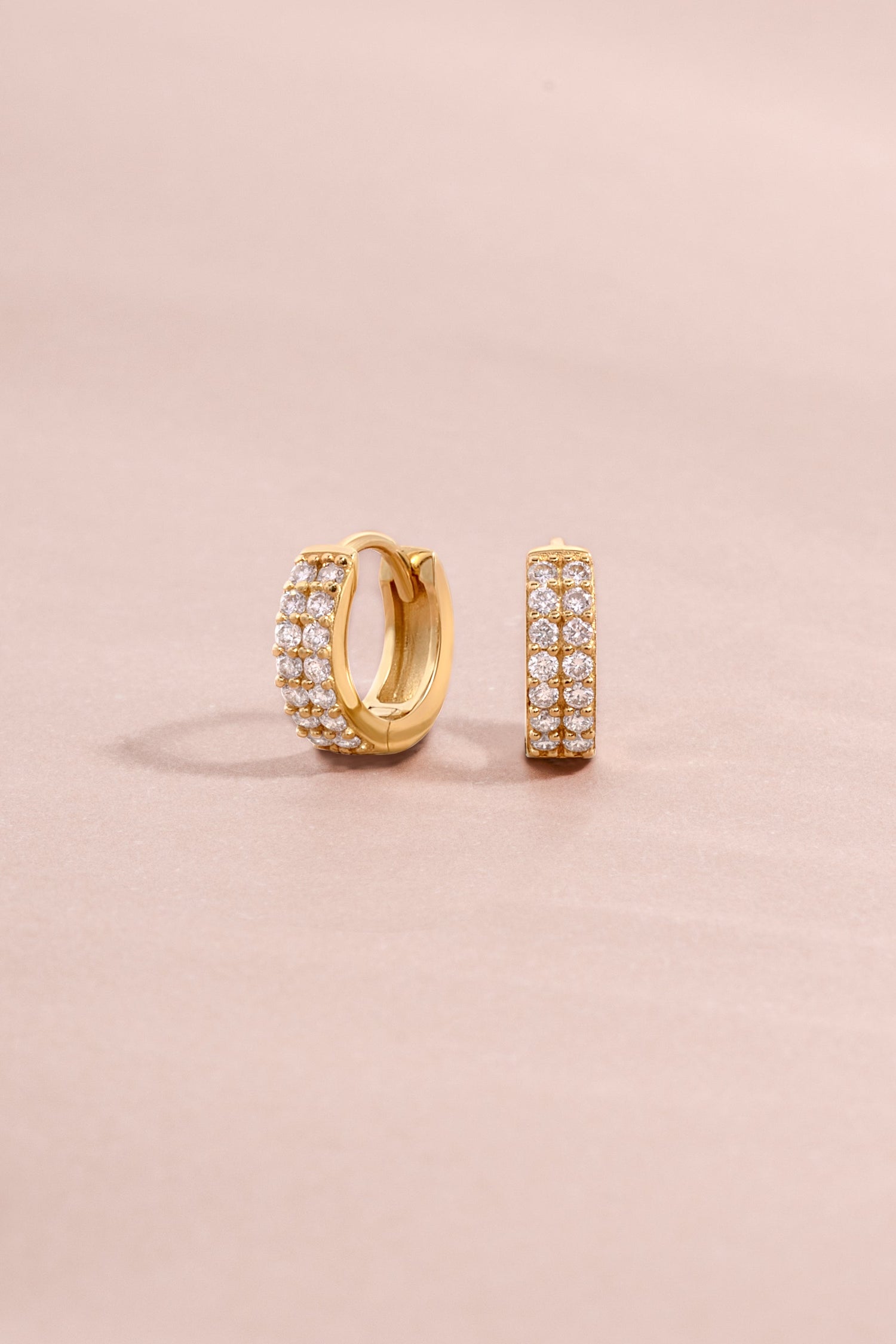 Solid 14K gold hoop earrings with two rows of diamonds on a light pink background