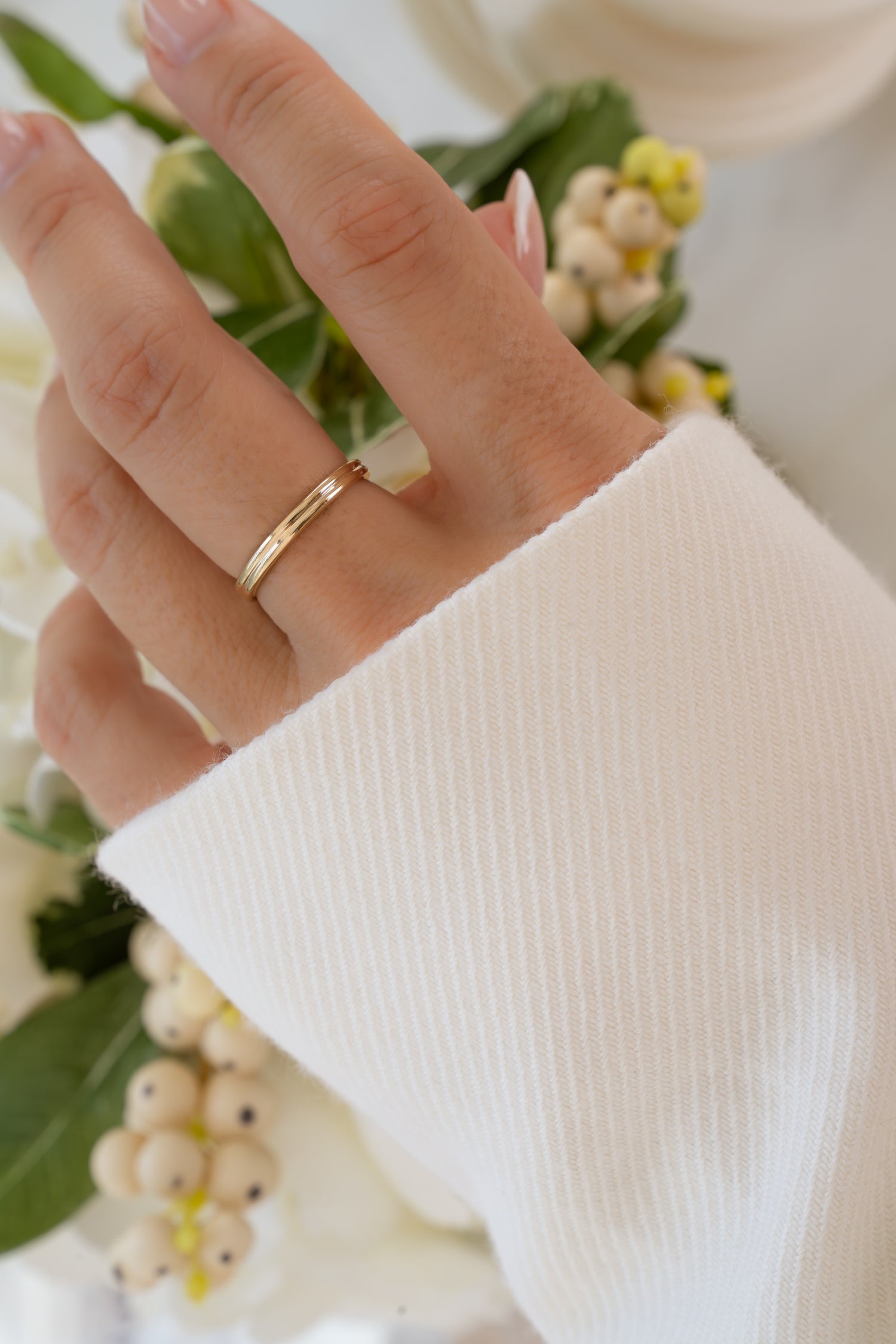 Hand wearing a 14K solid gold double band ring with a blurred floral background