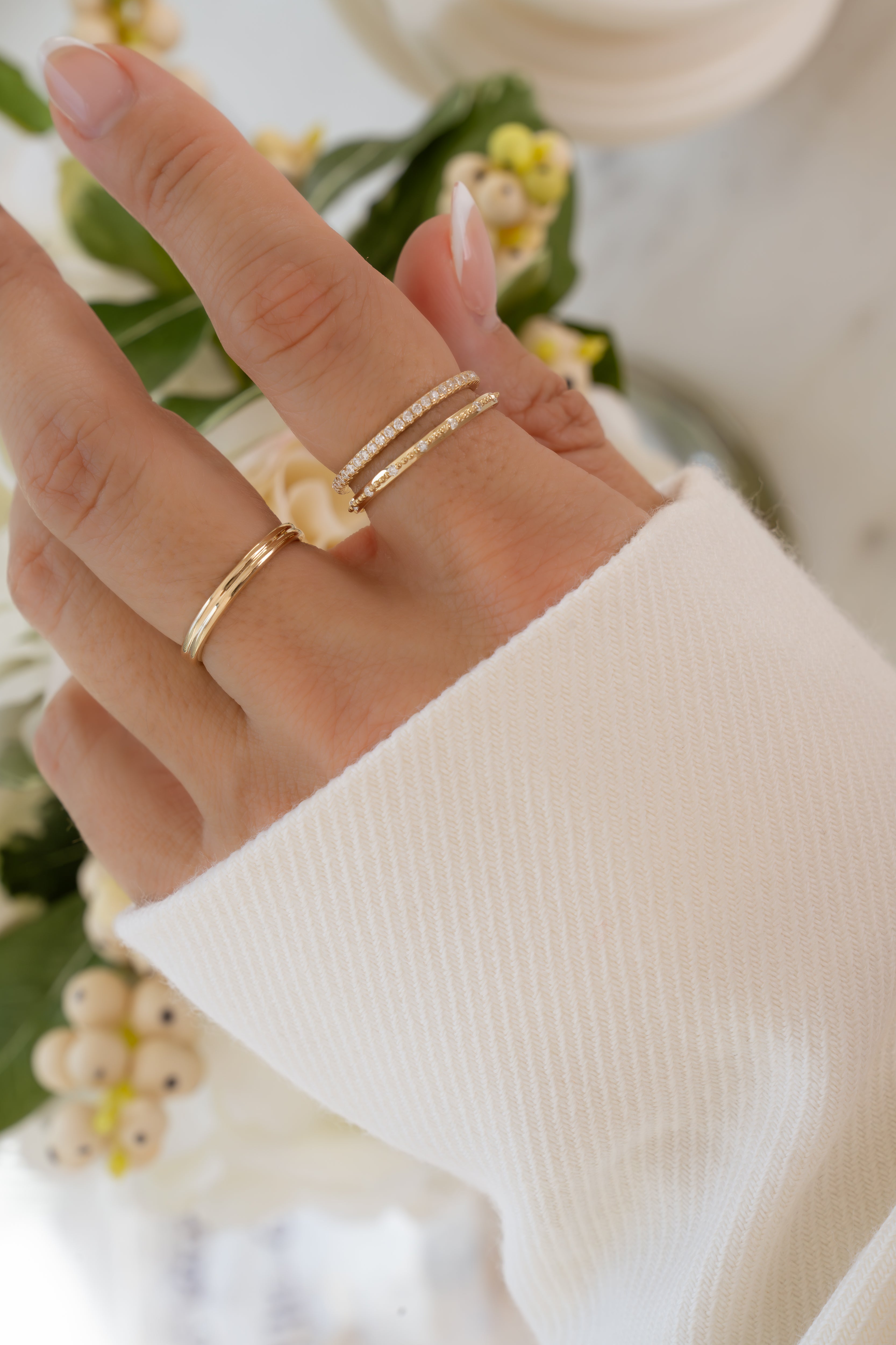 Hand wearing three 14K solid gold rings with lab grown diamonds styled with a blurred floral background