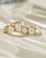 Close-up of gold Bella 3 Stone Huggie Hoops earrings by Sami Jewels, featuring three sparkling stones in a hoop design.