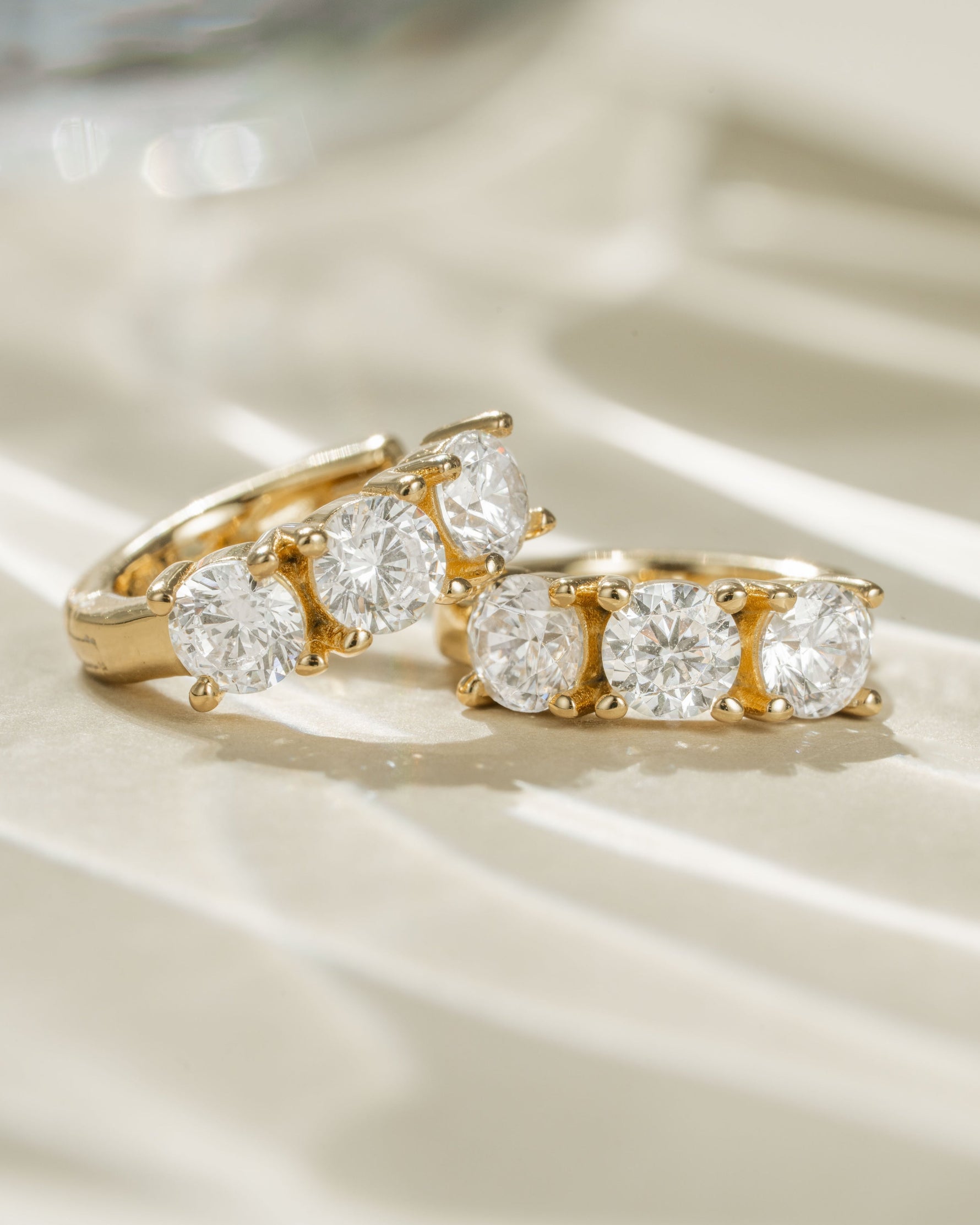 Close-up of gold Bella 3 Stone Huggie Hoops earrings by Sami Jewels, featuring three sparkling stones in a hoop design.
