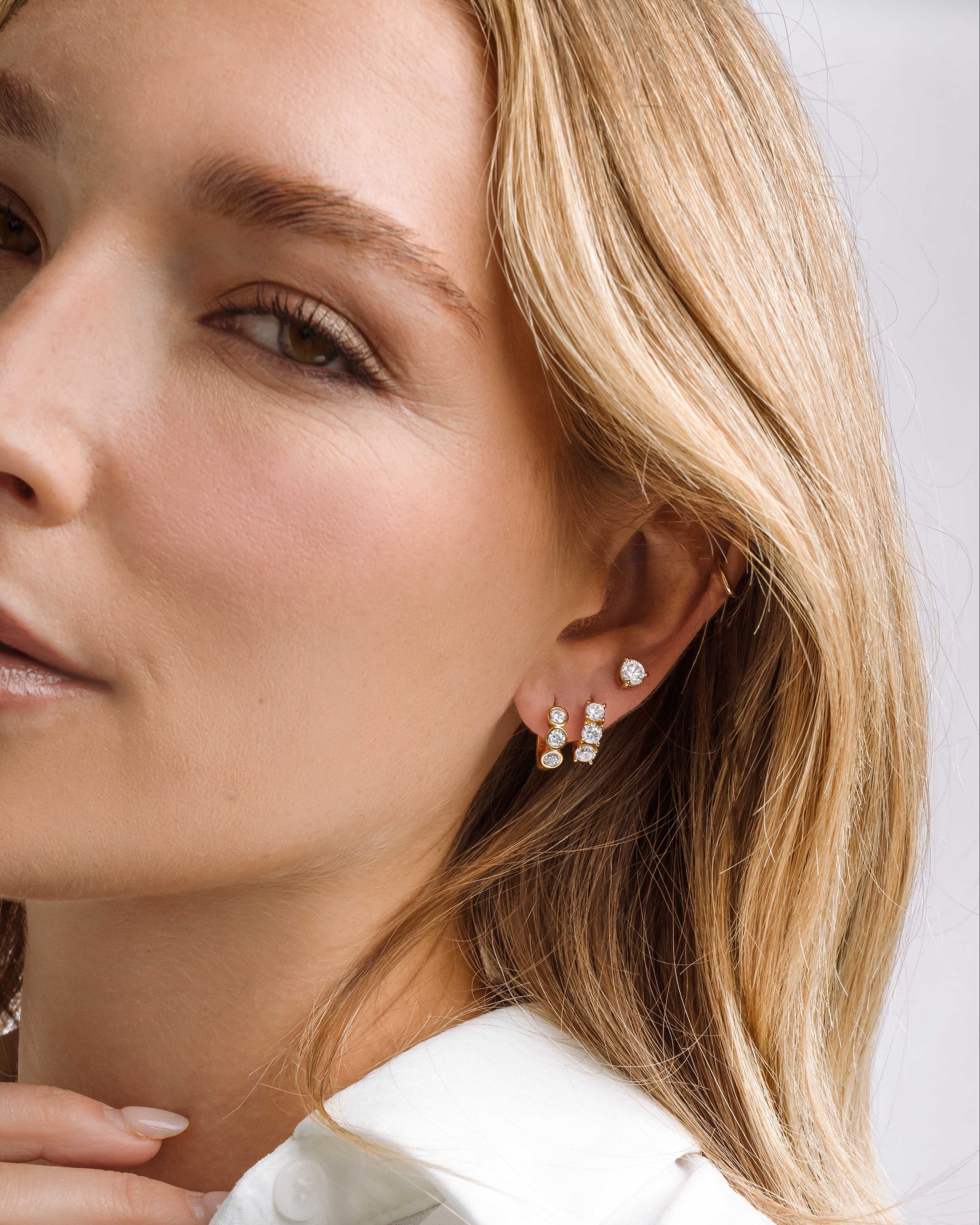 Gold Bella 3 Stone Huggie Hoops earrings by Sami Jewels, featuring three sparkling stones on small hoop earrings.