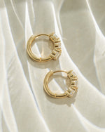 Gold Bella 3 Stone Huggie Hoop Earrings by Sami Jewels, showing a profile view with three sparkling stones on each hoop.