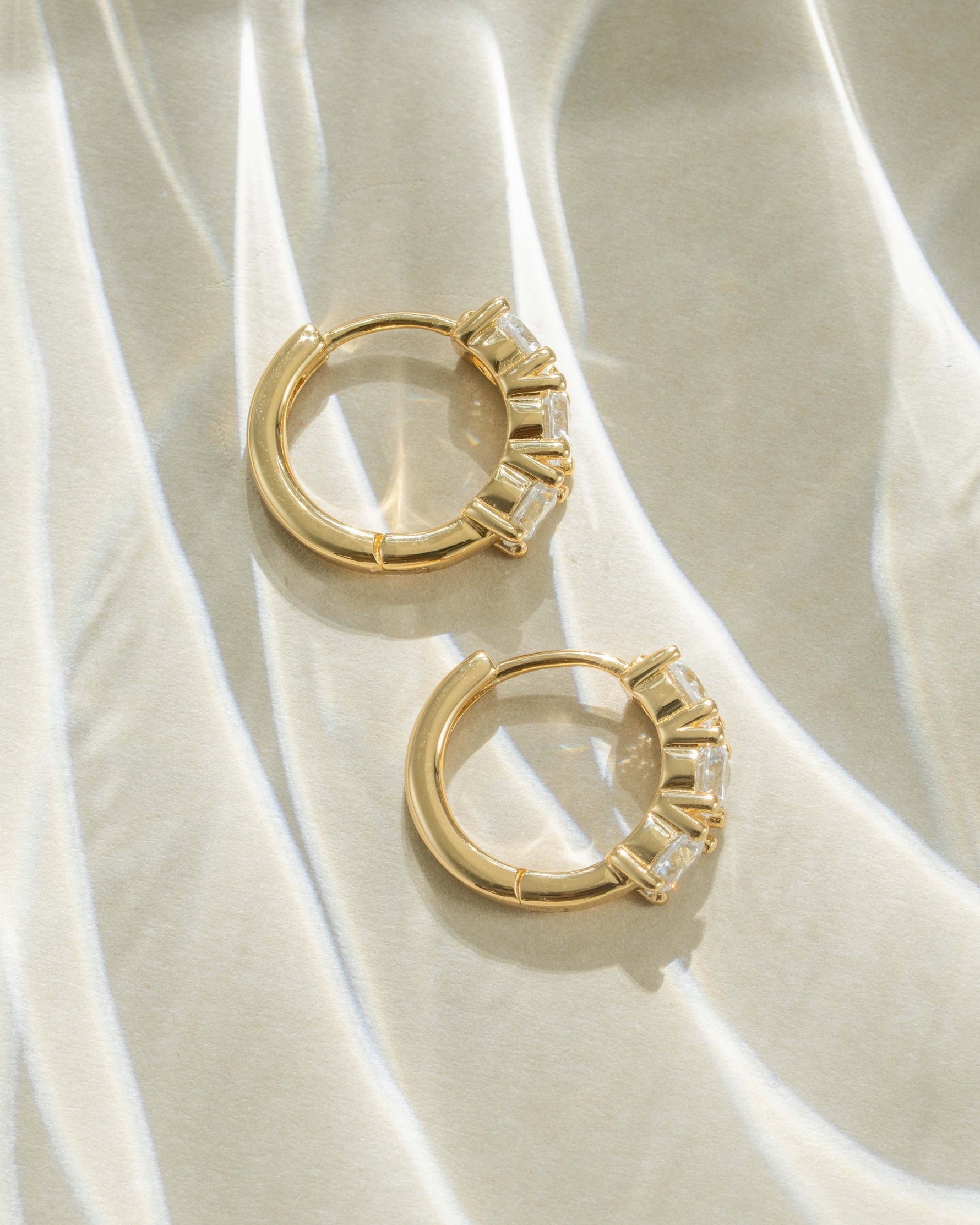 Gold Bella 3 Stone Huggie Hoop Earrings by Sami Jewels, showing a profile view with three sparkling stones on each hoop.