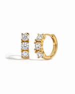 Gold Bella 3 Stone Huggie Hoops earrings with white background, featuring three sparkling stones and a secure hoop design.