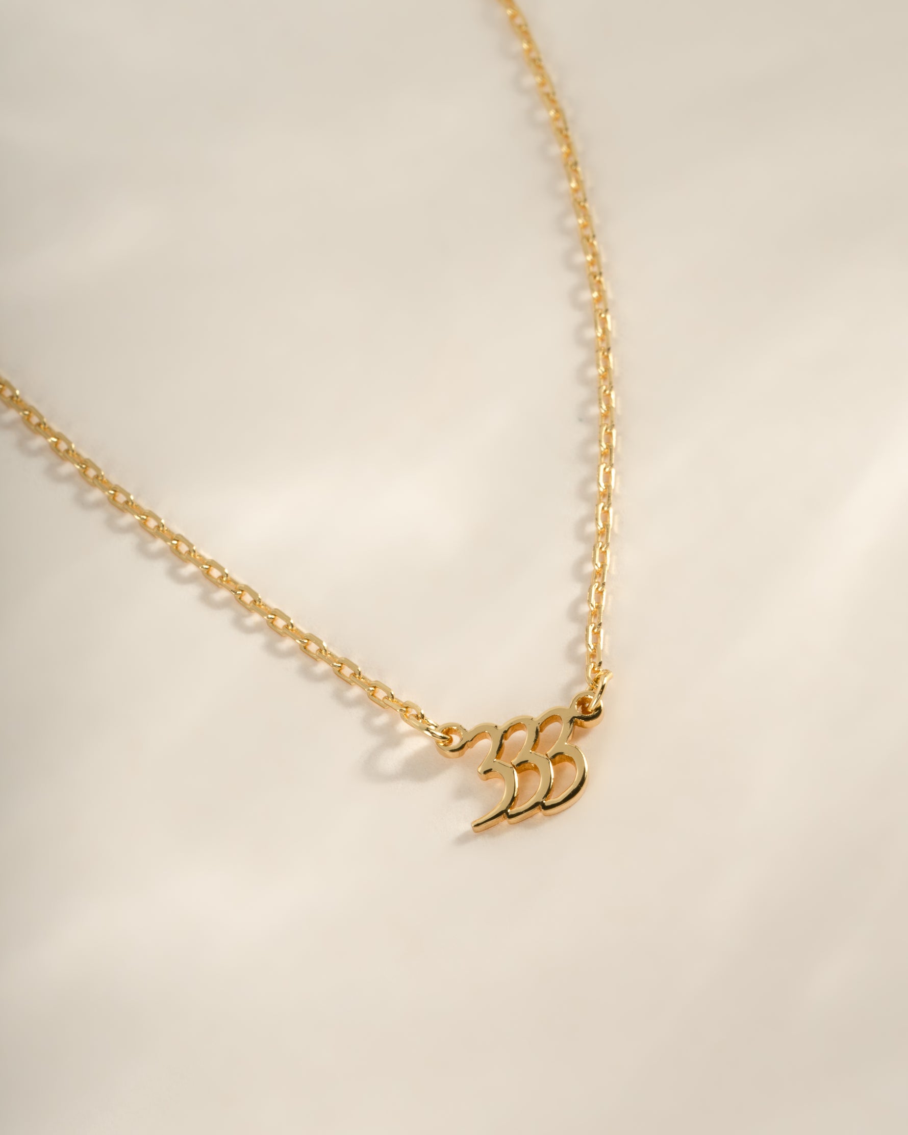 Close-up of Sami Jewels gold angel number 333 necklace showing detailed number pendant on a chain.