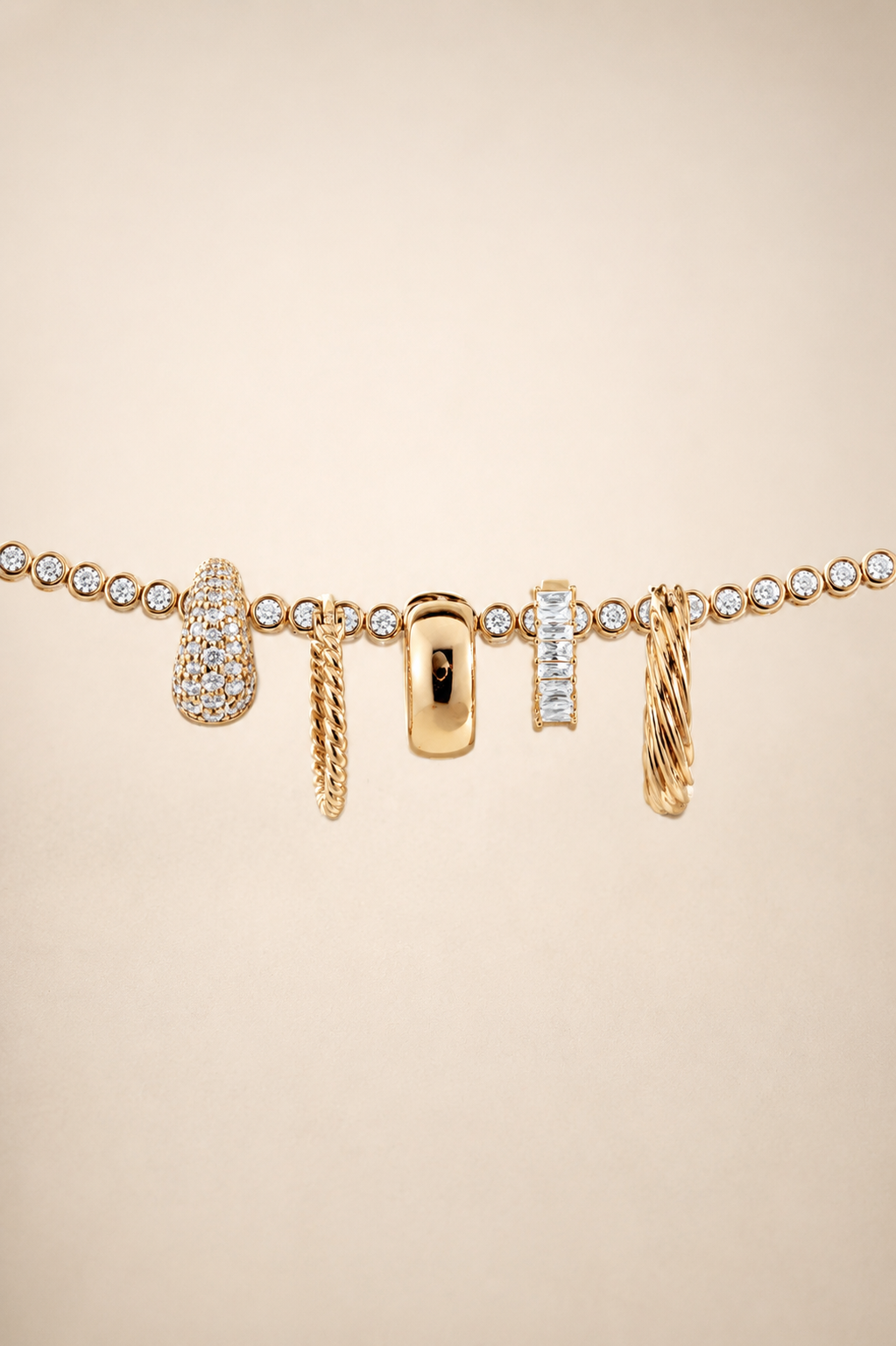 A gold-tone charm bracelet featuring multiple dangling charms, including a pear-shaped pavé charm, a twisted rope charm, a rectangular pavé charm, and a twisted cable charm, displayed on a warm beige background.
