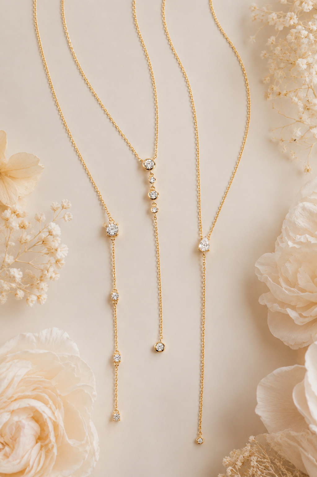 a flat-lay image of three gold dainty lariat y-necklaces with white flowers surrounding them.