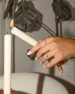 Hand lighting a candle with another candle in the background, with gold stackable rings on model 