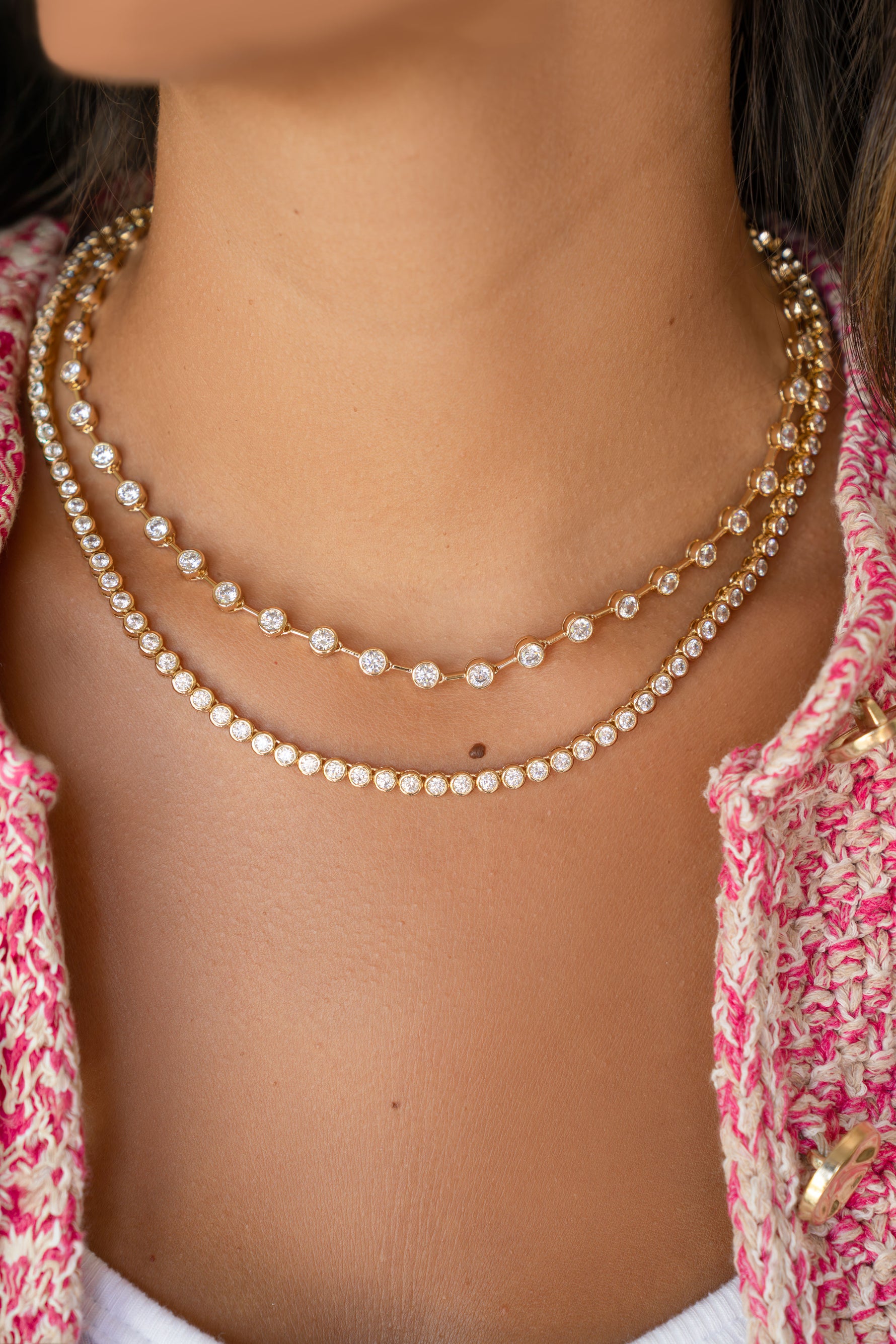 Close-up of a person wearing two tennis necklaces with a pink patterned top.