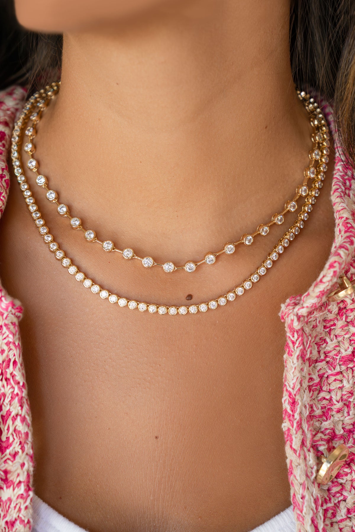 Close-up of a person wearing two pearl necklaces with a pink patterned top.
