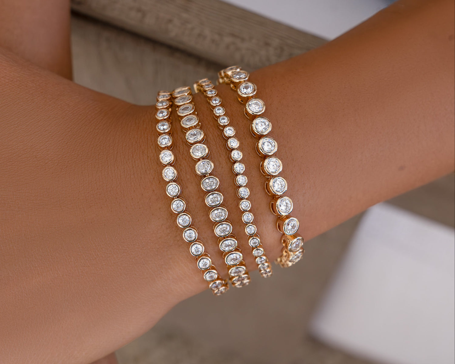 Close-up of a wrist wearing multiple gold and diamond bracelets on a blurred background