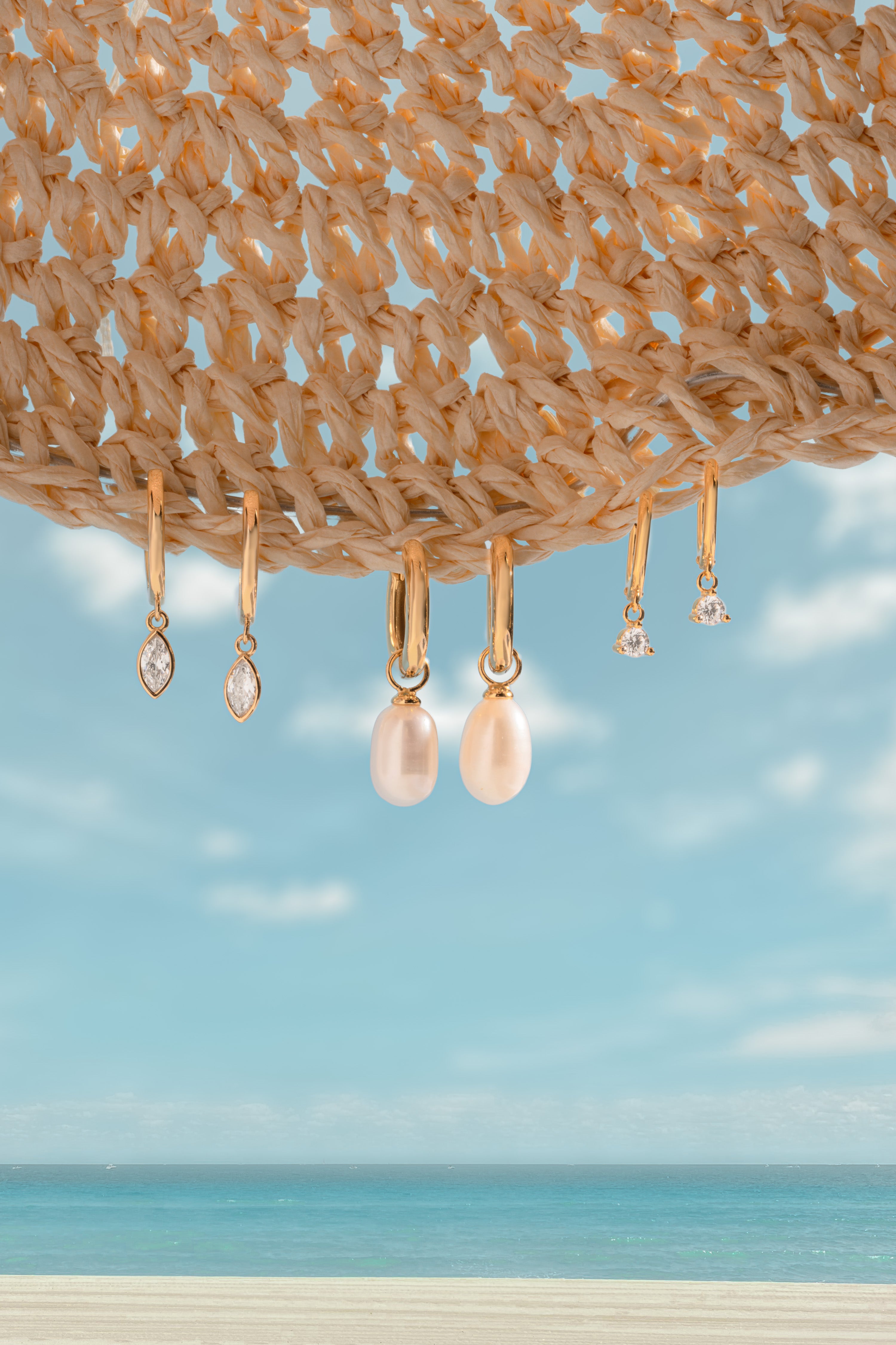 Pearl earrings hanging from a woven basket against a blue sky and ocean background