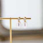 closeup image of pearl dangle drop earrings with a cubic zirconia bezel set stone on an earring holder