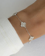 Silver charm bracelet with clover designs on a wrist against a white background