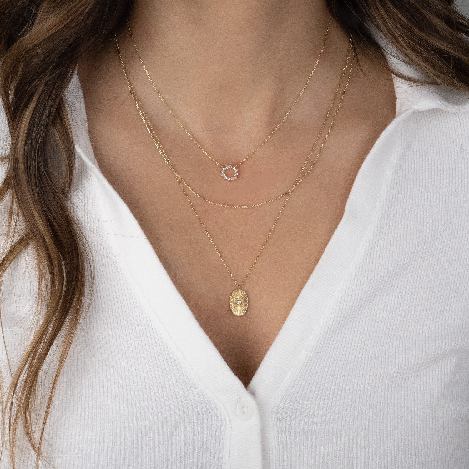 Layered look with sunburst pendant necklace on model and other dainty delicate gold necklaces