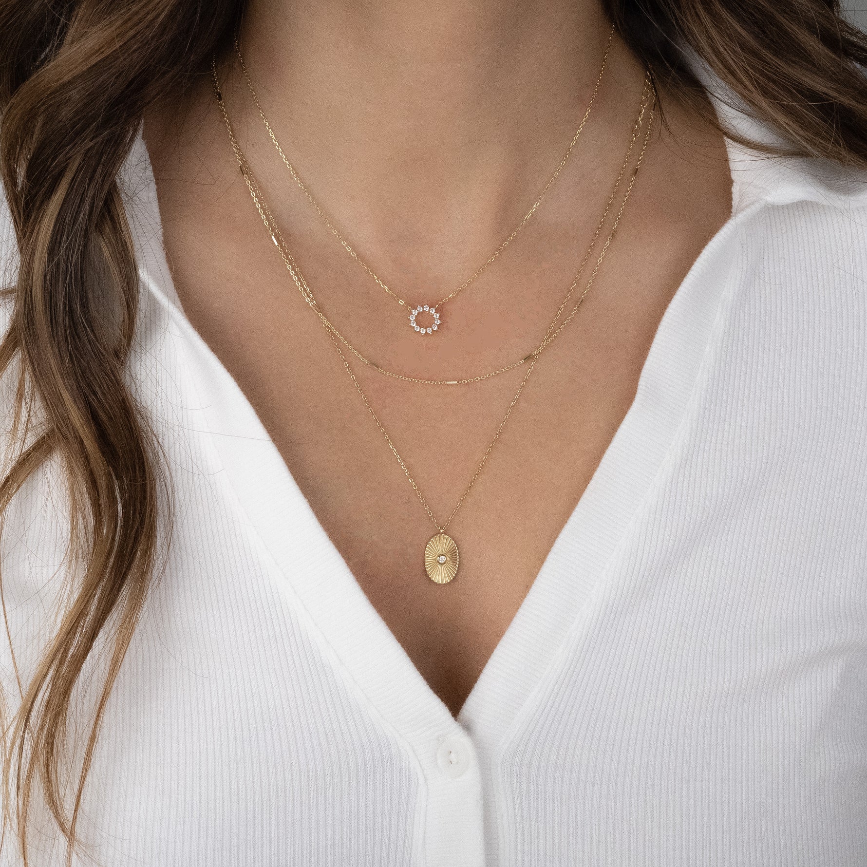 Layered look with sunburst pendant necklace on model and other dainty delicate gold necklaces