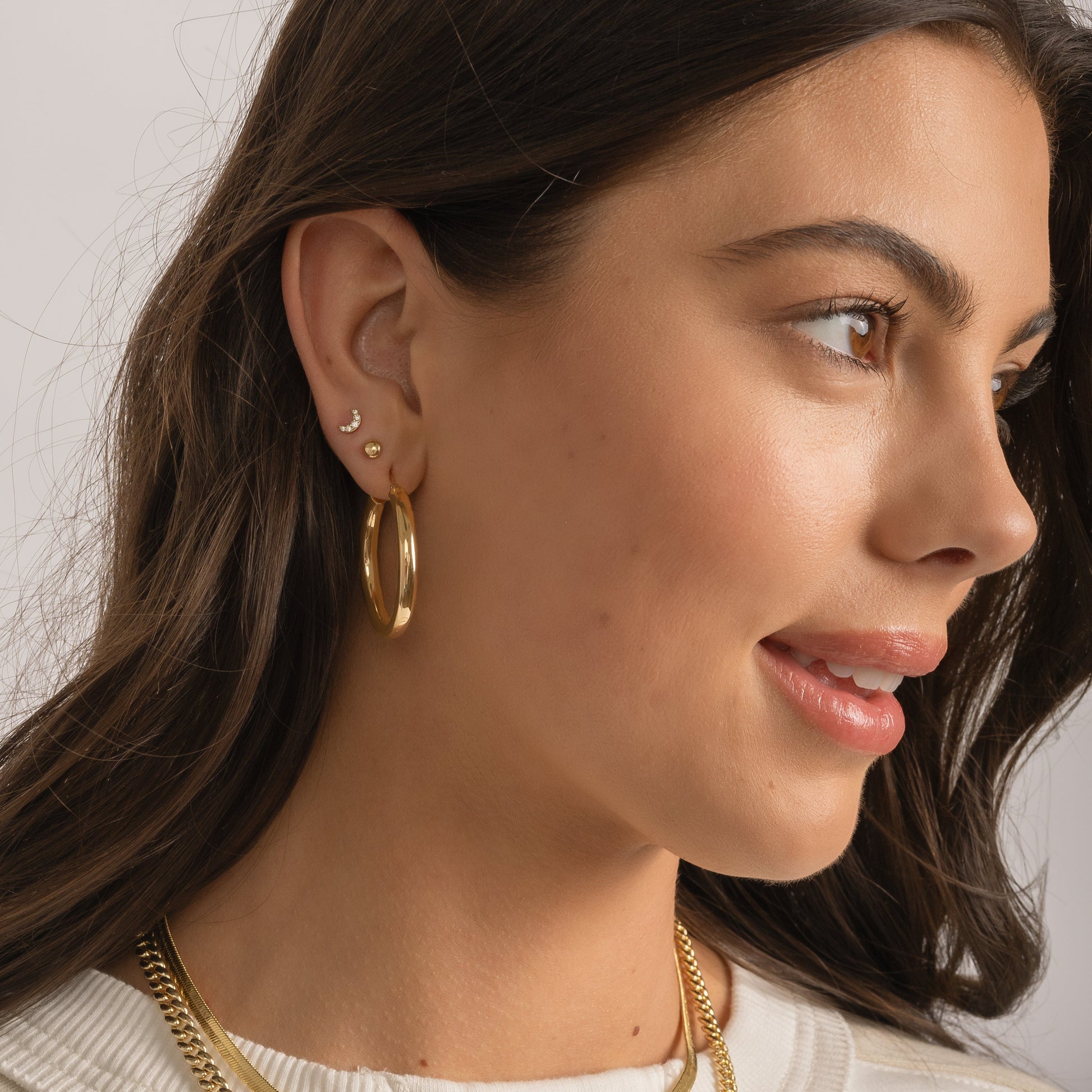 Model wearing dot studs, hoops, and gold moon studs with other gold jewelry from Sami Jewels.